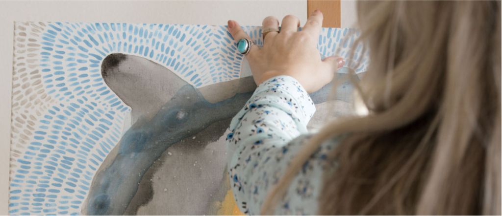 A zoomed-in shot of Elanni placing a textured painting on an easel.